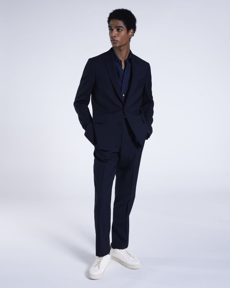a male model wearing a full designer navy suit with shirt and white trainers