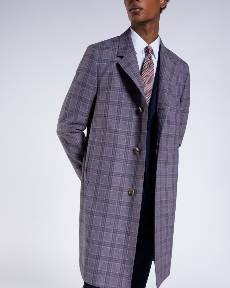 a male model wearing a navy business suit paired with a long checked overcoat