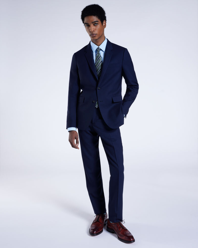 a male model wearing a navy business suit with a striped tie and formal brown brogues
