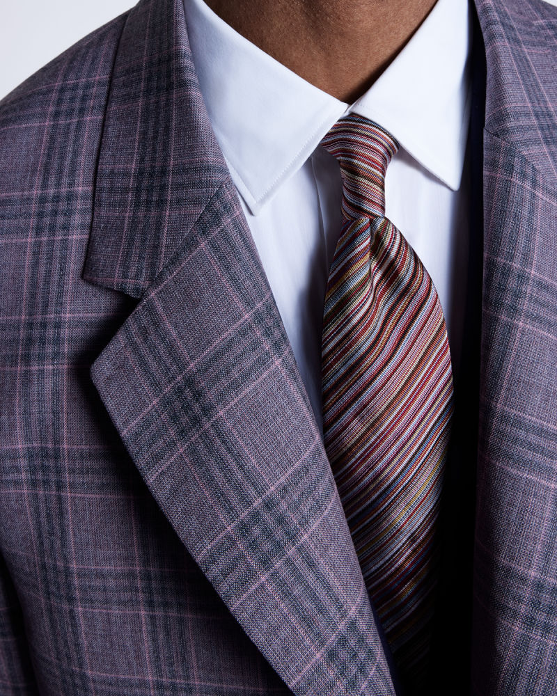 a male model wearing a statement striped tie, paired with a white shirt and checked overcoat