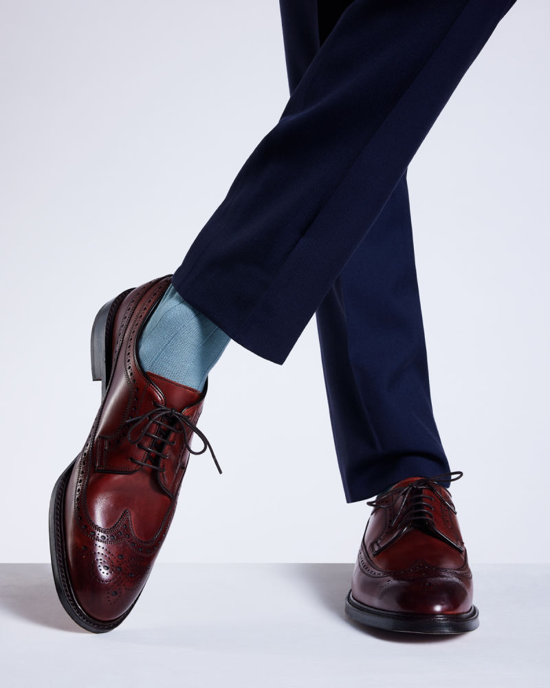 a male models lower leg wearing navy suit trousers with brown brogues