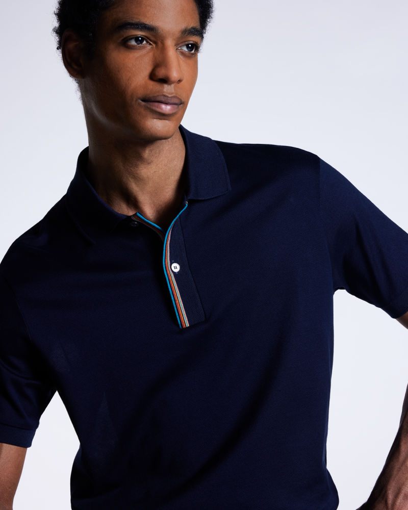 a male model wearing a navy polo shirt with a colorful stripe detail on the collar opening