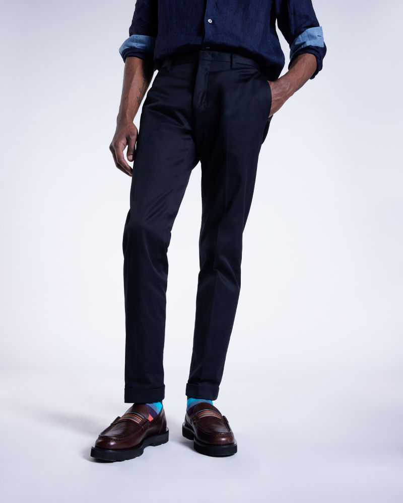 a male model stood with one hand in his pocket, wearing navy shirt and trousers with light blue socks and brown loafers