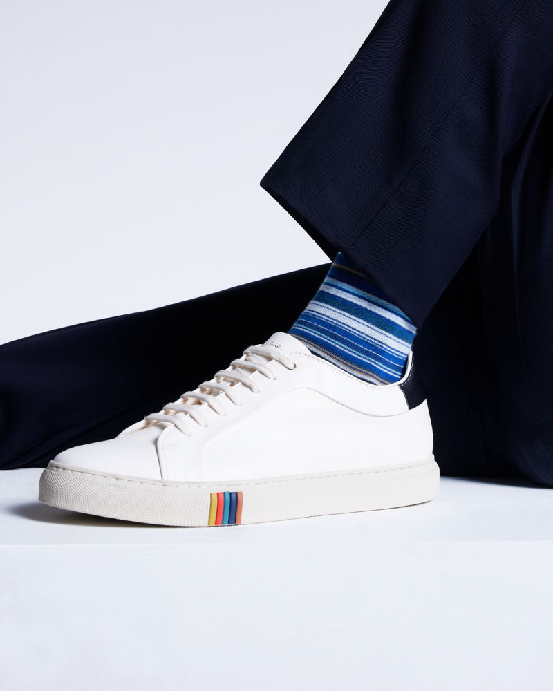 a male models legs wearing navy trousers and blue striped socks, paired with white trainers with a colourful stripe pattern on a section of the midsole