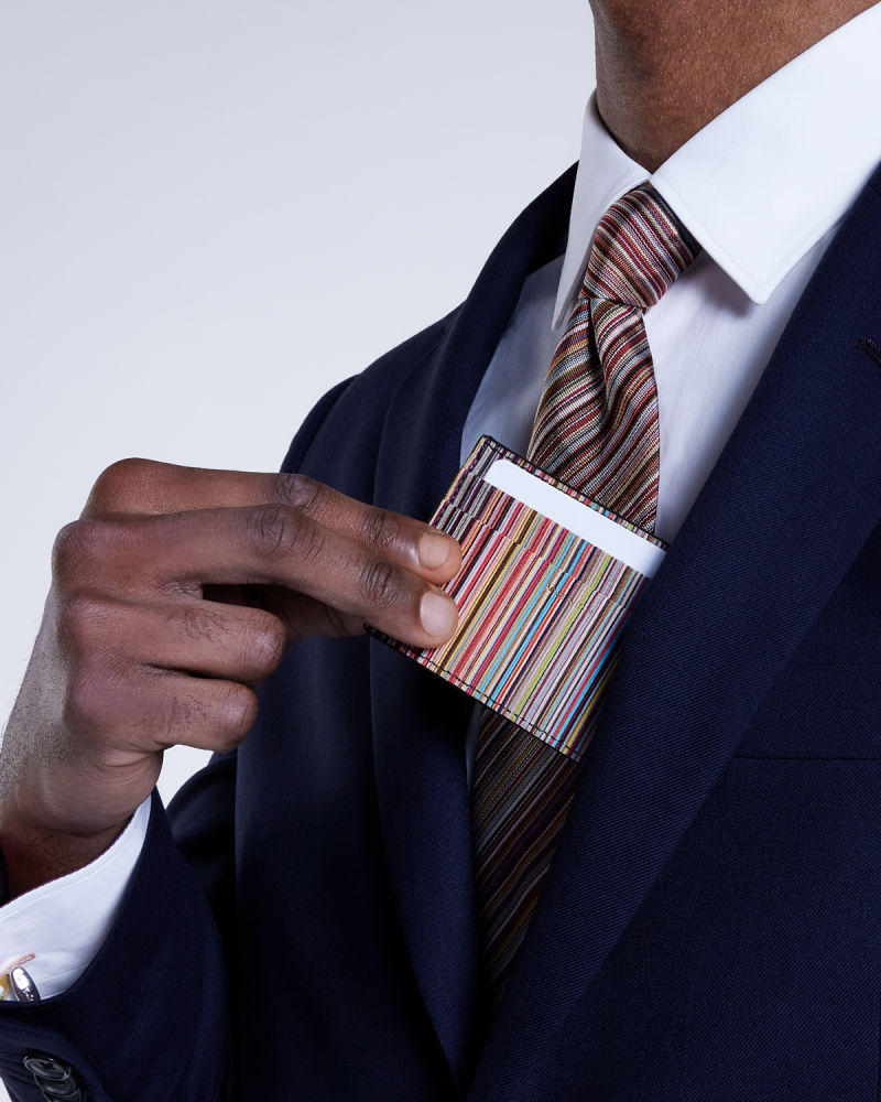 a male model wearing a navy business suit paired with a colourful striped tie, pulling a striped cardholder from the inside suit pocket